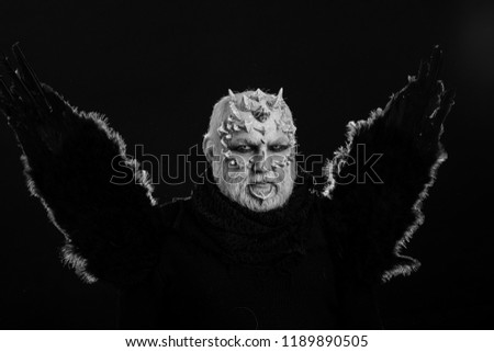 Man with black bird wings on dark background. Demon with raven or crow feathers. Wizard with thorns and horns on skin. Dragon with white eyes and beard on face. Magic and mystery concept.