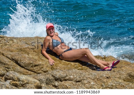 A beautiful girl poses on a rock and enjoys in waves