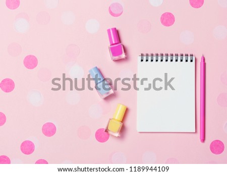 Empty note book and colorful nail polishes on pink confetti background. Copyspace for text. Bright and festive picture. Top view, flat lay.