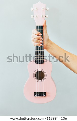 Woman hand with fashion manicure holding little pink ukulele on grey background. Fine female musician picture.