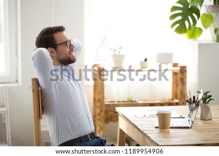 Relaxed glad businessman or business owner holding hands behind head with closed eyes smiling in office at workplace. Concept of successful deal, good job and end of the working day no stress at work Royalty-Free Stock Photo #1189954906