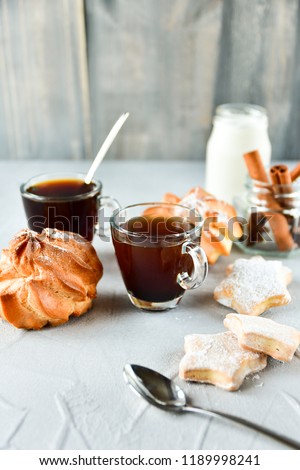  Breakfast: two cups of black coffee in transparent cups, milk and round eclairs with cream filling "crème brûlée", biscuits and cinnamon sticks with glass jar. homemade Breakfast in bed
