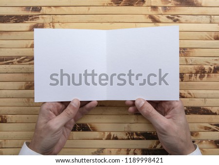 Mens hands holding empty white booklet on bamboo background. View from above