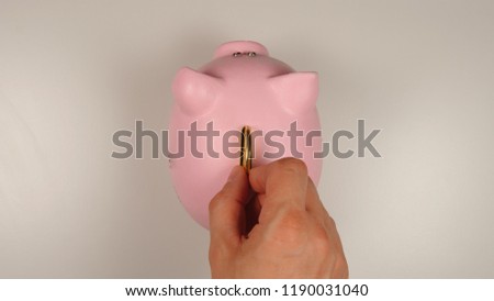 TOP VIEW: Human hand throws a coin into pink pig money box