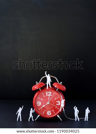 miniature paper people with  a large clock, an alarm clock on a black background. The concept of time and man