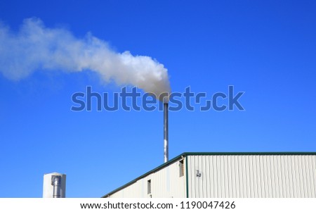 Metal chimney with white smoke against blue sky