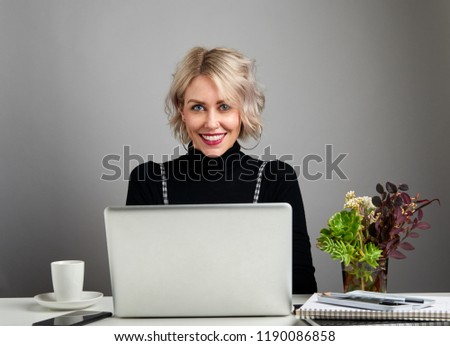 Attractive smiling young woman with a laptop sitting at a desk looking at the camera with joy, happiness and excitement.