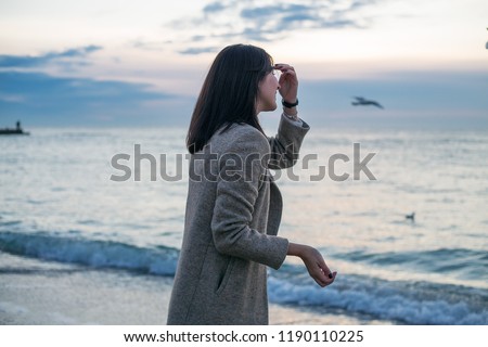 Brunette girl in winter coat looking to the sea against beautiful sea sky background, stylish wear, skin care, brunette hipster enjoy the sea, happy model, dreamer, girl in white shirt, laugh,bohemian