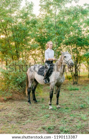 Beautiful young girl  with light hair in uniform competition smiling and astride a horse in sunset in autumn
