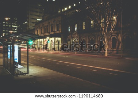 View of traffic light lines on road in blur with empty bus stop on pavement in night time, Brisbane