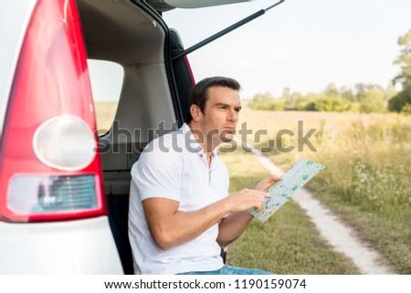 lost man sitting in car trunk and navigating with map in field