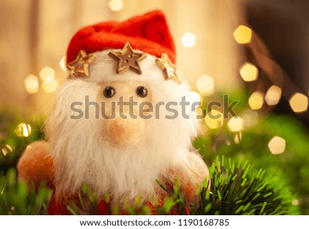 Christmas toy Santa Claus in a cap with тримя gold stars among green tinsel against the background of the shining garland
