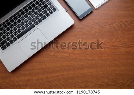 Wood office desk table with laptop, glasses, notebook, pen, smartphone. Top view, copy space.
