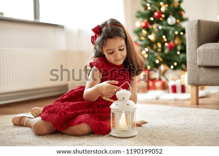christmas, holidays and childhood concept - happy little girl playing with lantern at home