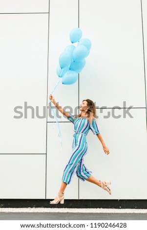 a playful and pretty woman with colorful outfit flying with her blue baloons