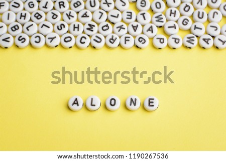 The word ALONE made of white plastic blocks on yellow background with many letters on the top