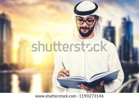 Arab teacher, professor, student writing at his notebook, in dubai, uae background