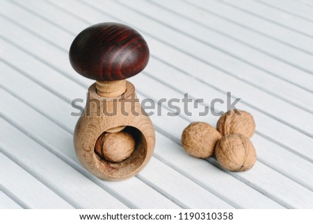 Wooden nutcracker in a shape of mushroom. Perfect for cracking nuts. Lovely decoration in addition. Screw type nut cracker with walnuts on white wooden background 
