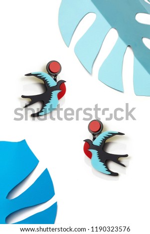 Close up top view of two colourful swallow birds isolated on white background, framed with blue Monstera leaves. Nature-inspired design accessories. Exotic style women jewelry. Summer vacation theme.