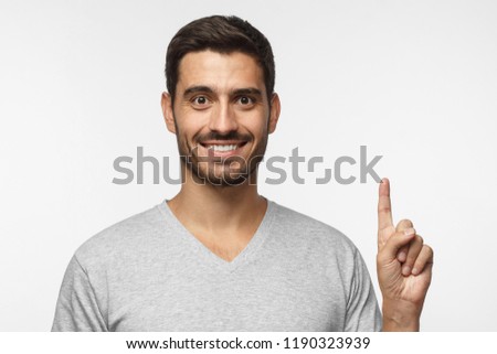 Handsome young man pointing up with his index finger, isolated on gray background