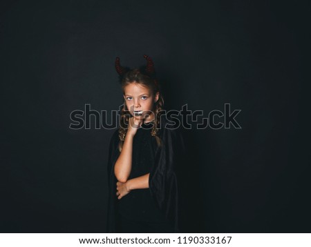 beautiful young girl with red halloween horns and cape in front of black background