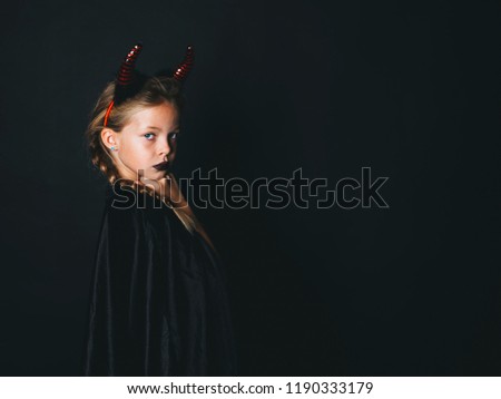 beautiful young girl with red halloween horns and cape in front of black background
