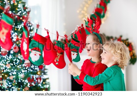 Kids opening Christmas presents. Child searching for candy and gifts in advent calendar on winter morning. Decorated Christmas tree for family with children. Little girl and boy in Xmas pajamas.