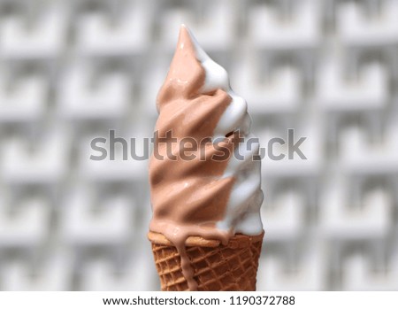 Melting Vanilla and Chocolate Flavors Soft Serve Ice Cream Cone with Blurred Modern Pattern Concrete Wall in Background