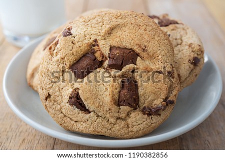 Pile of chocolate cookies in white plate and a cup of milk on wood table, macro picture