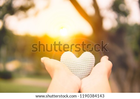 Hands are hold a blue  heart in the evening to replace the love in the Valentine.Have background in garden and light of sun. 