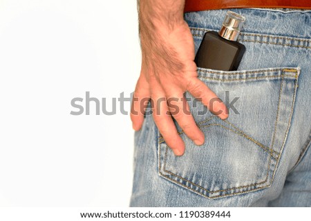 Hand resting on the back pocket of a blue jeans with a bottle of perfume inside.