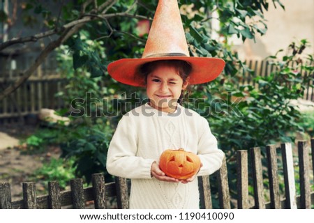 Happy Halloween . Girl with pumpkin and hat on the street . The child is holding a lantern made of pumpkin