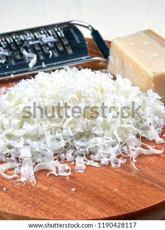 A heap of freshly grated parmesan, on a wooden board, and a parmesan grater