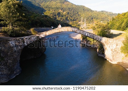 A girl is sitting on an ancient stone bridge. Georgia.