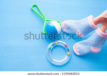 Baby yellow booties. Children's shoes in women hands and toys on blue background. Newborn. Top view