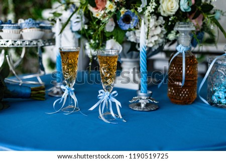 a festive table with a blue tablecloth: two glasses and a decanter with an alcoholic drink, flowers, cakes, a candle