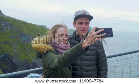Two young people take photos and selfies at the Kerry Cliffs