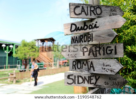 Street signs in the natural park indicating directions to different places of the world. On the background two person walking. Taken in north Italy.