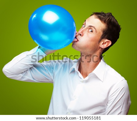 Portrait Of Young Man Blowing aÃ?Â Balloon On Green Background