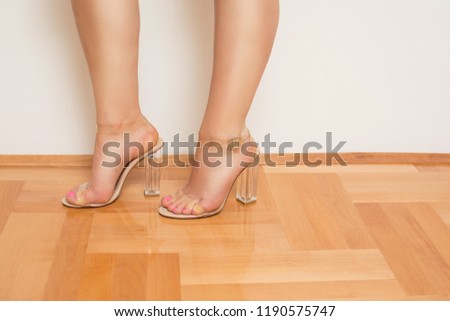 Young female feet in transparent sandals. Modern female high heel see-trough shoes. Studio lighting, medium retouch.