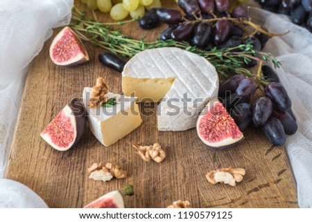 Cheese soft camembert with mildew with oregano branches on a dark wooden background with grapes, fig tree and walnuts