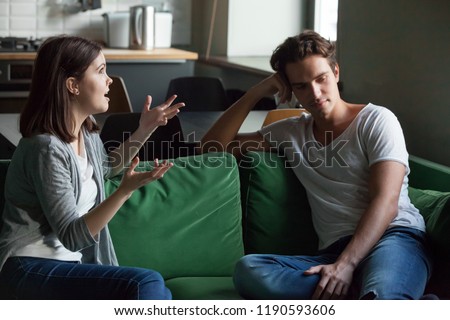 Young attractive couple sitting on couch at home and sorting out their relations. Girlfriend talking too much, drama queen nagging disinterested boyfriend feels angry. Troubles and break up concept Royalty-Free Stock Photo #1190593606
