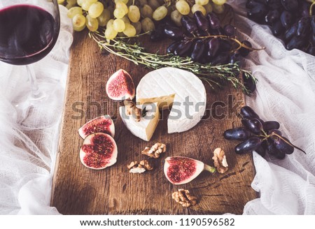 Top view on a wooden tray there is an assortment of camembert cheese along with sliced ​​figs and grapes