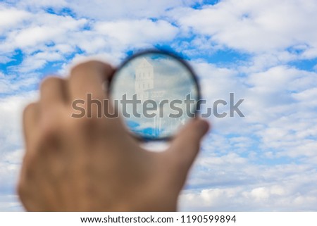 photography hobby concept creative foreshortening of reflection from temple building in camera lens polarizing filter in human hand on blue sky with clouds background, copy space