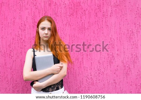 Portrait of attractive redhead girl holding tablet pc and looking at camera isolated on pink background. Fun lifestyle and technology concept. Copy space in right side