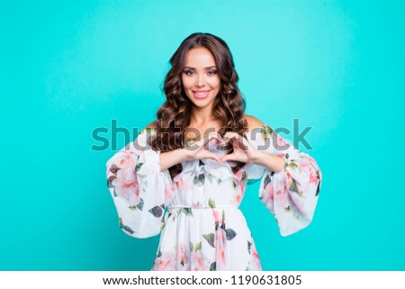 Portrait of dreamy, charming, lovely, sweet, gorgeous curly brunette showing love symbol, heart shape with fingers, looking at camera isolated on vivid teal background