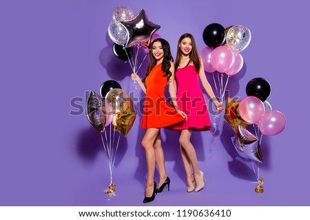Two fancy, rich people in fuchsia, red formalwear, casual clothes on sharp, pumps, stilettos look at camera stand isolated on vivid violet background with air helium blow decoration in hands