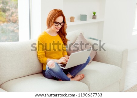 Photo of beautiful, attractive, pretty, dreamy, charming, lovely person in casual yellow sweater pullover, denim jeans using gadget in modern light interior on cozy, comfort couch