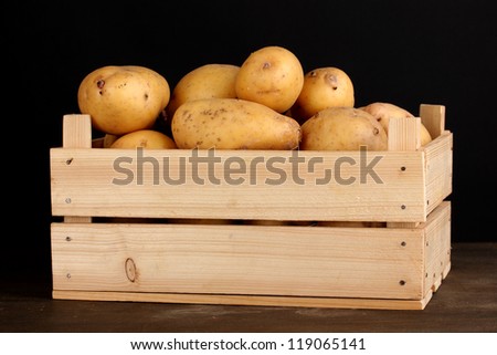 Ripe potatoes in wooden box on wooden table on black background