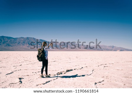 Young hipster girl with backpack using mobile phone for taking photo of breathtaking scenery of death valley explore wild nature in trip, female travel blogger making picture on cellular in Badwater